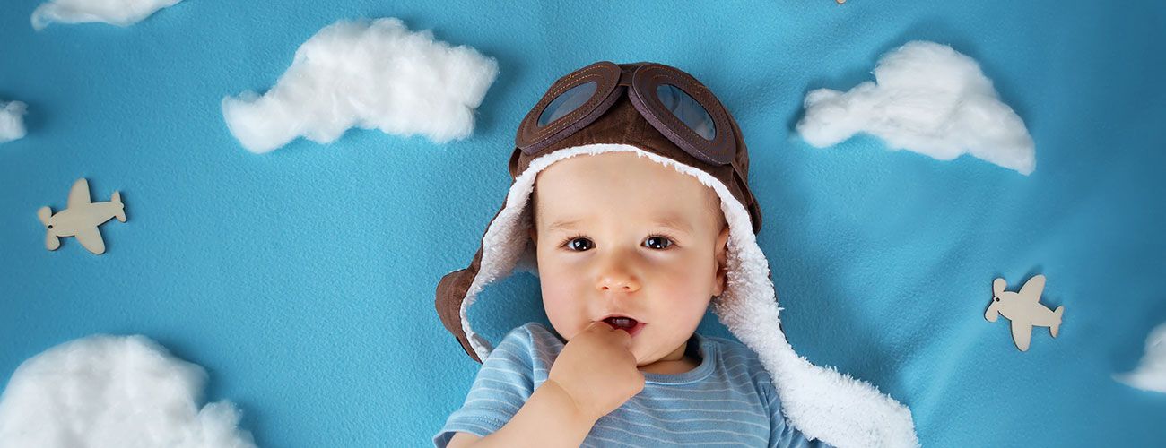 Baby in front of cloud background wearing pilot goggles